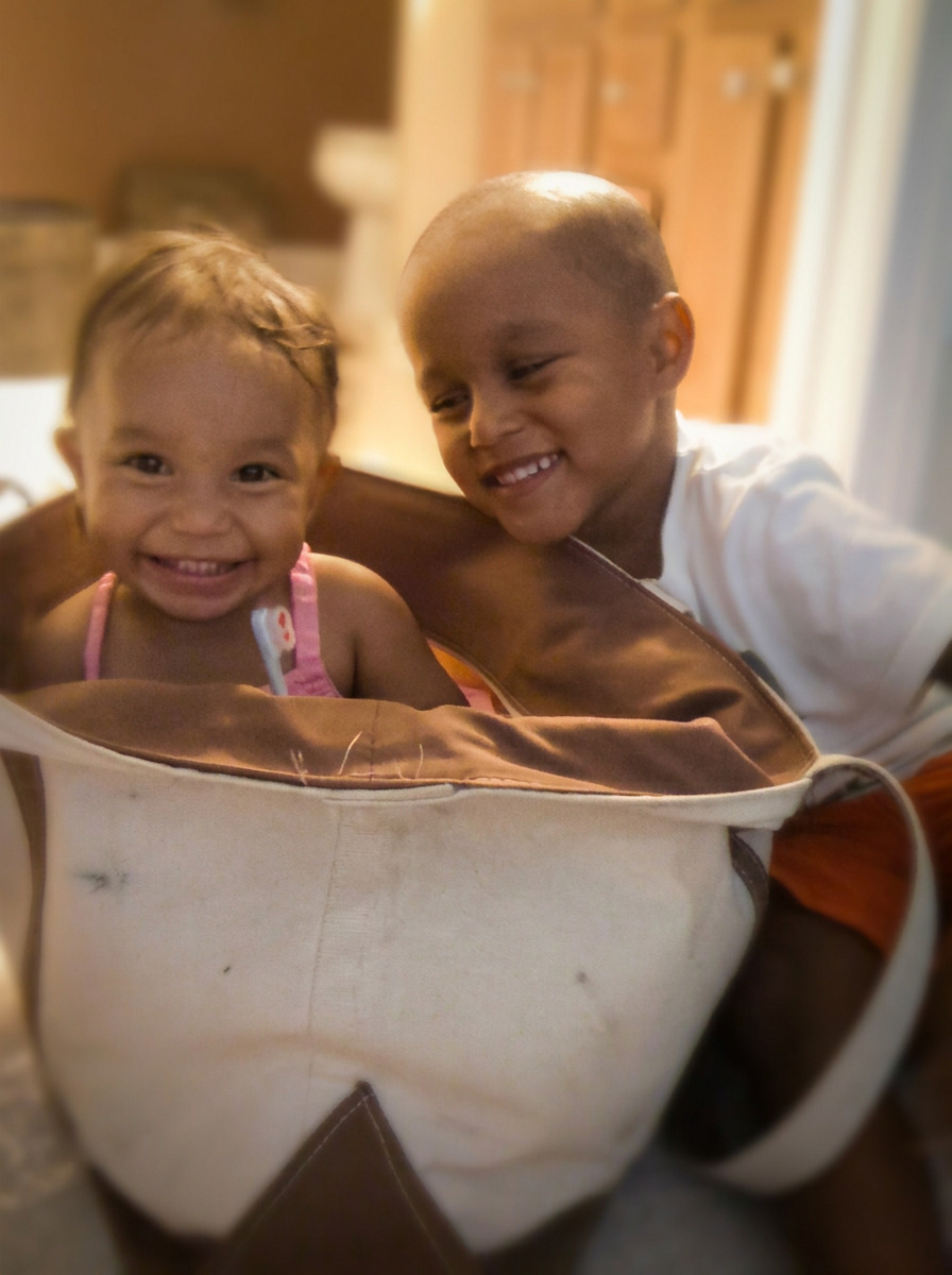 Two smiling young children sitting close together in a soft basket
