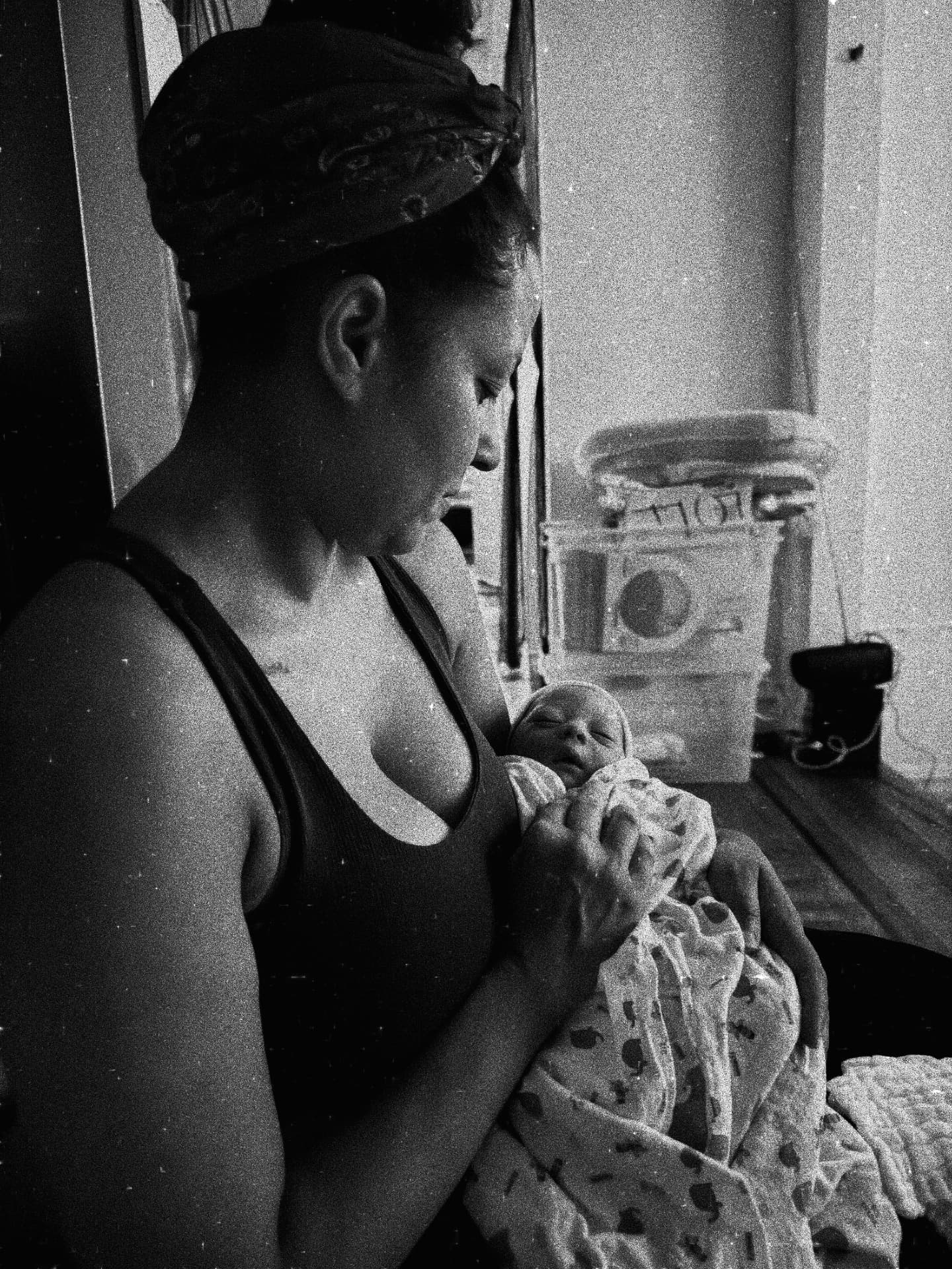 Hazel Alvarez (Nuna) holding a swaddled newborn in soft window light